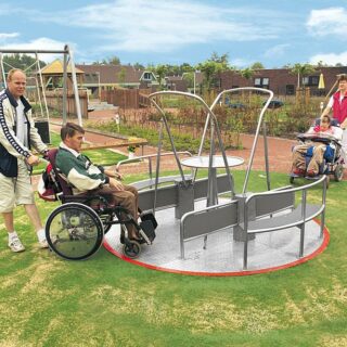 Accessible play equipment - Two wheelchair users are pushed onto the integration carousel.