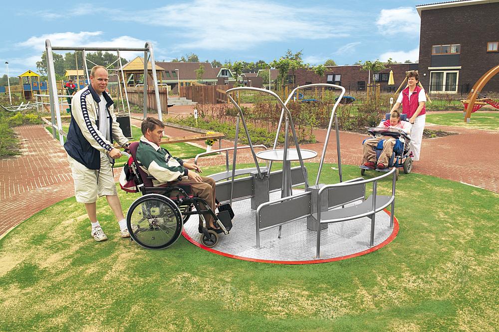 Accessible play equipment - Two wheelchair users are pushed onto the integration carousel.