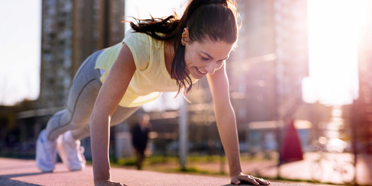 Calisthenics - a woman in sportswear does push-ups outdoors.