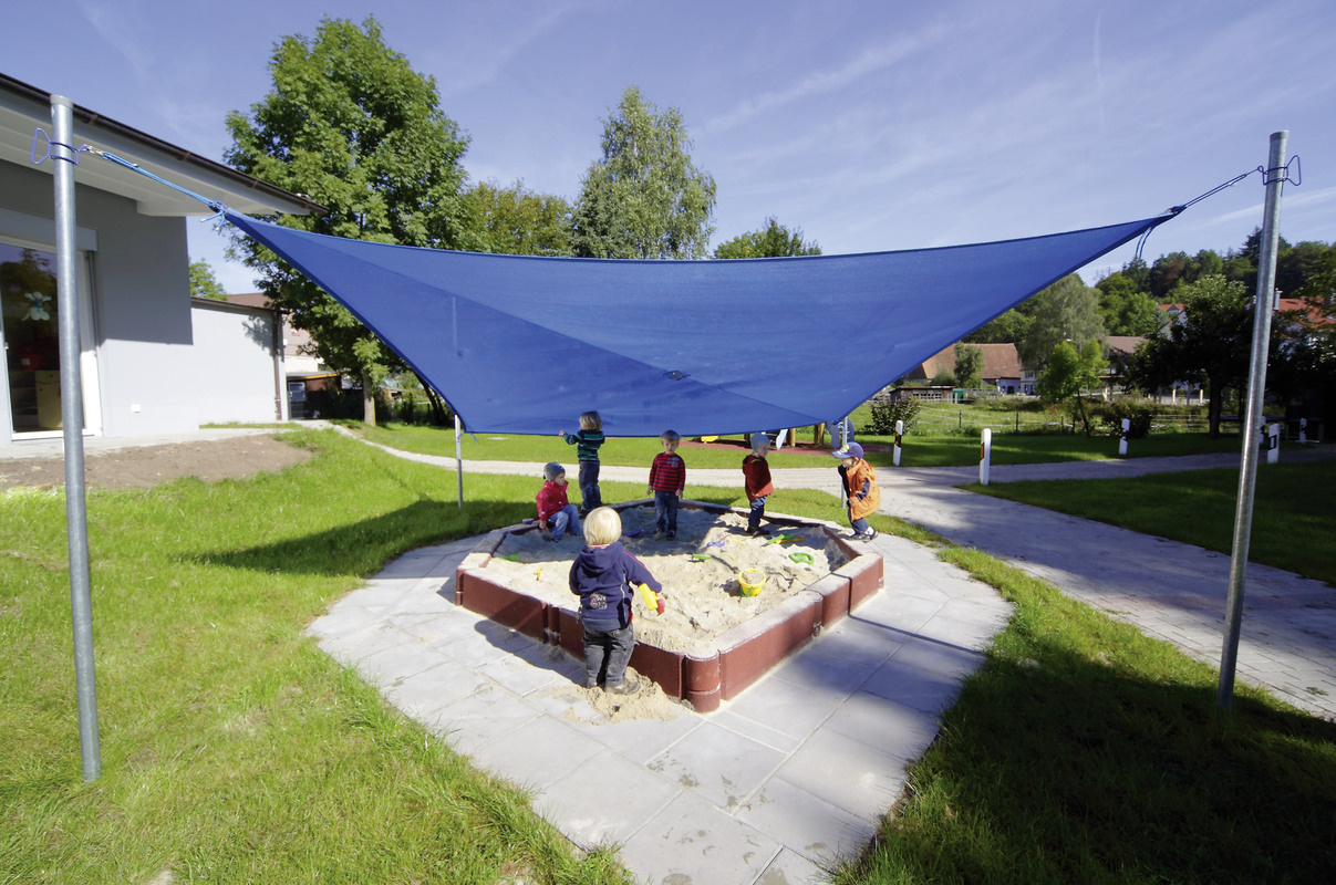 Sandpit with sunshade – Blue sun sail stretched over sandpit with playing children.