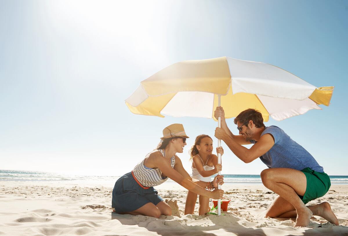 Sandbox with awning - mother, father and daughter build up a parasol on the beach.